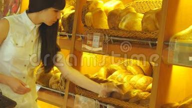女人选择并把一个新鲜的面包放进超市的包裹里。 小女孩拿着一条面包
